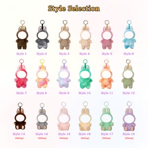 Pu&ograve; includere: Una collezione di diciotto portachiavi a forma di coniglietto di peluche in vari colori, ciascuno con un'apertura circolare per una foto. I portachiavi sono disposti in file, con il testo "Style Selection" in alto.