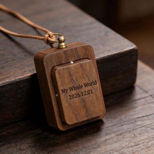 May include: A rectangular wooden pendant with a hinged front, engraved with the text "My Whole World 2026.12.01". The pendant is attached to a brown leather cord with a knot and a brass-colored metal clasp.