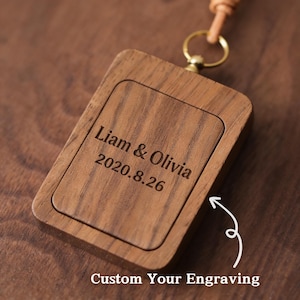 May include: A rectangular wooden keychain with rounded corners, featuring engraved text: "Liam & Olivia 2020.8.26". The keychain has a leather strap and a gold-colored metal ring. The text "Custom Your Engraving" is below the keychain.