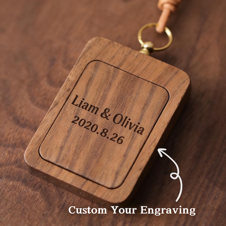 May include: A rectangular wooden keychain with rounded corners, featuring engraved text: "Liam & Olivia 2020.8.26". The keychain has a leather strap and a gold-colored metal ring. The text "Custom Your Engraving" is below the keychain.