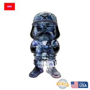 May include: A blue and white figurine of a stern-faced character wearing a cap and uniform. The figurine has its arms crossed and is standing. The word "HBOH" is in a red box in the upper left corner. The figurine is handmade in the USA.