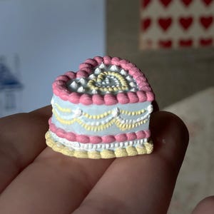 Peut inclure: Un gâteau en forme de cœur avec un glaçage rose, des décorations dorées et blanches, et une base jaune. Le gâteau est tenu dans une main. Le texte "digital file" est dans une bannière.