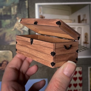 May include: A miniature wooden chest with a hinged lid, black metal accents, and a small handle. The chest is brown with visible wood grain and is open, revealing the interior. The image also includes the text "digital file" on a banner.