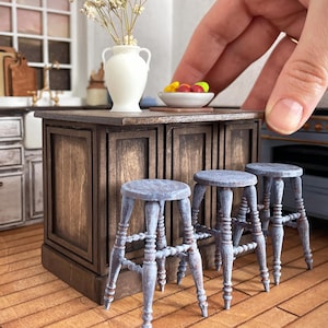 Op de afbeelding: Miniatuurkeuken met een houten eiland, drie blauwe krukken en een witte vaas met gedroogde bloemen. Een kleine fruitschaal staat op het eiland. De afbeelding bevat de tekst "digital file" in een banner.