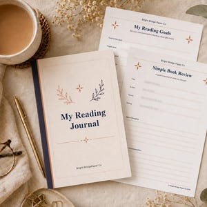May include: A reading journal with a cream cover, dark blue text reading My Reading Journal, and two matching printed inserts titled My Reading Goals and Simple Book Review. The journal features small star and leaf illustrations in dark blue and orange.