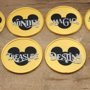May include: Eight yellow coasters with a black Mickey Mouse head silhouette and a word in white script. Words include Dream, Wonder, Magic, Fantasy, Wish, Treasure, Destiny, and Adventure. The coasters are on a wooden surface.