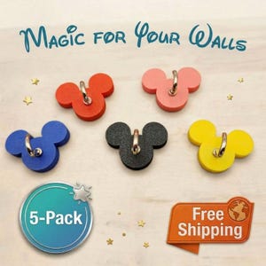 May include: Five colorful wall hooks shaped like a famous mouse character. The hooks are red, pink, blue, black, and yellow. Each hook has a silver-colored ring for hanging. The text "Magic for Your Walls" is at the top.
