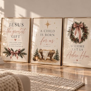 May include: Three framed wall art prints featuring Christmas themes. The left print reads Jesus the greatest gift with pine branches and a pink bow. The centre print shows a manger with the text A child is born for us. The right print displays a wreath.