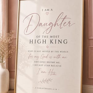 Puede incluir: Una lámina artística enmarcada con fondo crema y marco dorado. El texto dice: I AM A Daughter OF THE MOST HIGH KING WHO IS NOT MOVED BY THE WORLD for my God is with me AND GOES BEFORE ME; I DO NOT FEAR BECAUSE I am His. 2 CORINTHIANS 6:18.