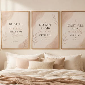 Puede incluir: Tres impresiones enmarcadas con citas inspiradoras. Cada impresión tiene un fondo beige claro con un diseño de estilo acuarela en tonos rosados. Las citas están en escritura elegante e incluyen frases como "Estate quieto" y "No temas".