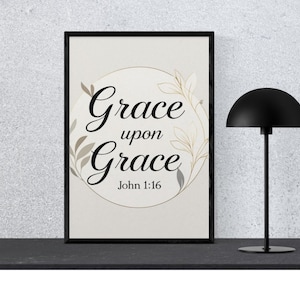 Op de afbeelding: Een ingelijste print met de woorden "Grace upon Grace" in elegant schrift, omringd door bloemaccenten. De tekst "John 1:16" staat eronder. Een zwarte lamp met een koepelvormige kap staat rechts.