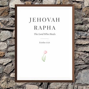 Puede incluir: Una impresión enmarcada con las palabras "JEHOVAH RAPHA" y "The Lord Who Heals" en texto negro. Una pequeña ilustración de tulipán en acuarela está en la parte inferior. El marco es marrón y el fondo es una pared de piedra.