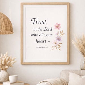Puede incluir: Impresión enmarcada con el texto "Confía en el Señor con todo tu corazón - Proverbios 3:5". La impresión presenta un marco de madera clara y detalles florales en rosa y morado. La obra de arte se exhibe en un salón.