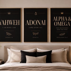 May include: Three framed art prints with gold lettering on a black background. The prints feature the words "YAHWEH", "ADONAI", and "ALPHA & OMEGA". Each print includes text and decorative elements. The prints are displayed above a bed.