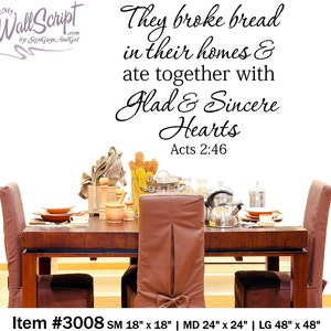 May include: A black and white wall decal with the quote "They broke bread in their homes & ate together with Glad & Sincere Hearts Acts 2:46". The decal is shown on a white wall above a wooden dining table with four chairs. The table is set with plates, silverware, and glasses. The decal is available in three sizes: 18 inches by 18 inches, 24 inches by 24 inches, and 48 inches by 48 inches.