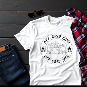 Może przedstawiać: Biała koszulka z czarną grafiką z napisem "OFF-GRID LIFE" wokół sceny kempingowej z górą i kamperem. Koszulka jest zestawiona z niebieskimi dżinsami, okularami przeciwsłonecznymi i czerwoną i czarną koszulą w kratę.