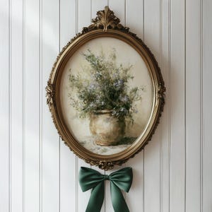 May include: An oval, gold-toned framed painting of a floral arrangement in a vase. The painting is hanging on a white, vertical-paneled wall. A dark green satin bow is tied below the frame. The frame has ornate detailing.