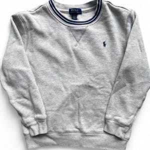 May include: A gray sweatshirt with a navy blue and white striped collar and the Polo Ralph Lauren logo. The long-sleeved crew neck sweatshirt has a small embroidered logo on the left chest.