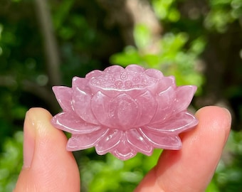 Pode incluir: Uma escultura de flor de lótus esculpida em pedra rosa, apresentando pétalas pontiagudas em camadas e um centro texturizado em forma de vagem. O objeto é translúcido com uma superfície lisa e polida, exibindo variações naturais no mineral.