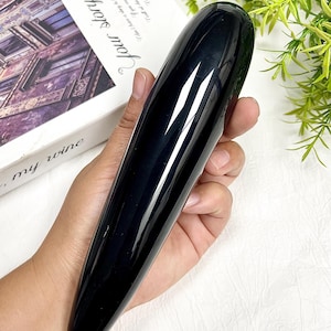 Peut inclure: Un objet cylindrique allongé et lisse avec une finition noire polie. L'article présente une extrémité arrondie et effilée ainsi qu'un aspect opaque et solide, reflétant la lumière sur sa surface incurvée. Il est tenu dans une paume.
