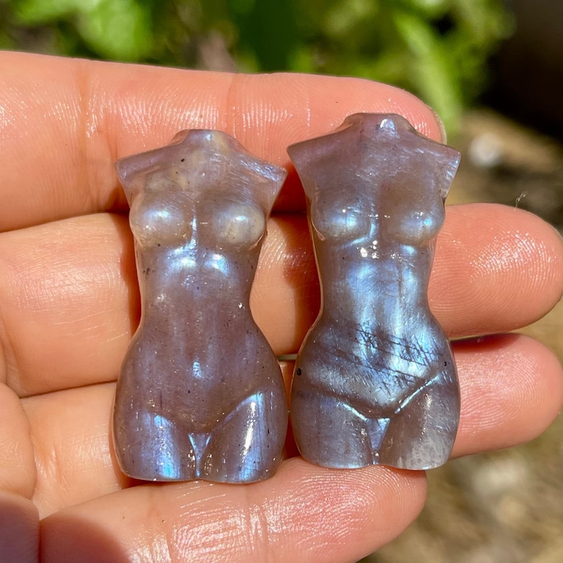 Pode incluir: Duas estatuetas esculpidas em pedra preciosa em forma de torso feminino. As est&aacute;tuas s&atilde;o uma mistura de roxo, cinza e azul com um brilho perolado. As figuras s&atilde;o lisas e polidas, com curvas definidas.