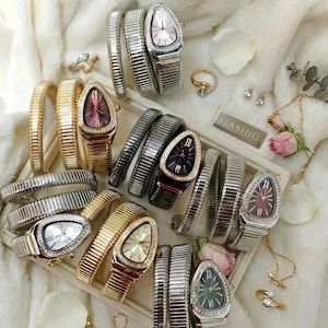 Puede incluir: Un surtido de relojes y pulseras de lujo en oro, plata y negro. Los relojes tienen esferas triangulares únicas con varios colores y adornos brillantes. La imagen también incluye anillos y un collar.