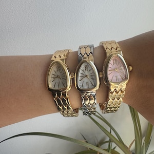 May include: Three wristwatches with triangular cases and textured, scale-like metal link bands. The left watch is gold-toned with a silver dial, the center watch is two-toned silver and gold with a silver dial, and the right watch is gold-toned with a pink dial.