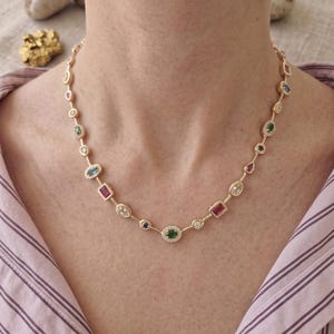 May include: A gold necklace featuring a selection of colourful gemstones, including emeralds, rubies, and sapphires. The necklace has a delicate chain and is decorated with oval, rectangular, and round-cut stones. The necklace is approximately 40 cm long.