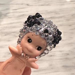Puede incluir: Peque&ntilde;a figura sonriente con tono de piel claro. La figura tiene una cabeza de cuentas negras y transparentes con forma de cristal. La figura tiene ojos negros y brazos extendidos.