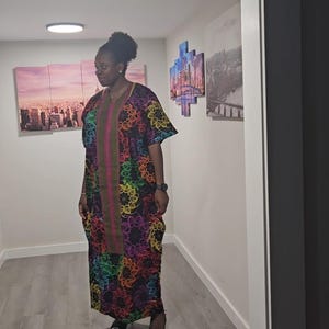 May include: A long, patterned dress in a variety of colours, with short sleeves and a central panel. The dress is worn with black heels. The dress's design features a repeating floral motif. The outfit is suitable for special occasions.