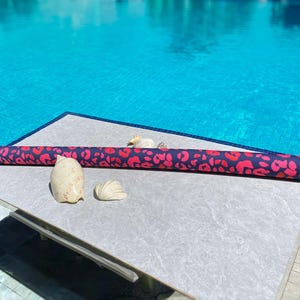 May include: A patterned pool float in blue and red lies near a swimming pool. Two seashells are placed beside the float. The pool water is a bright blue colour.