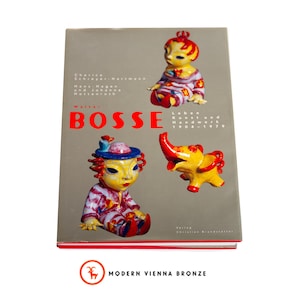 May include: A book titled "WALTER BOSSE" with illustrations of colorful ceramic figures. The cover features a seated figure, an elephant, and another seated figure. The book is on a gray background.