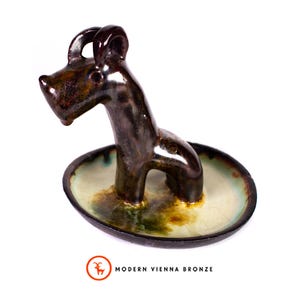 May include: A bronze-colored ceramic dog figurine with a glossy finish. The dog is emerging from a small, oval-shaped dish with a light green and brown interior. The Modern Vienna Bronze logo is visible.