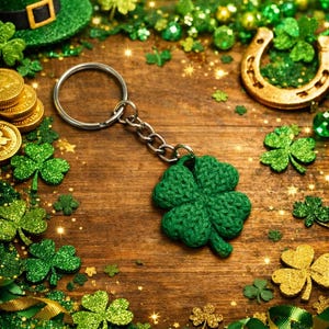 May include: A green crocheted four-leaf clover keyring sits on a wooden surface, surrounded by St. Patrick's Day decorations. Gold coins, a horseshoe, and shamrocks add to the festive theme. A green glitter top hat is in the background.
