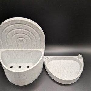 May include: A speckled gray soap dish set. The set includes a wall-mounted holder with a rainbow design and a small, matching dish. The holder has three drainage holes. The design is modern and minimalist.