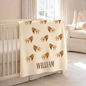 May include: Cream-colored baby blanket with a repeating pattern of watercolor lion illustrations. The blanket is draped over a white crib and features the name "WILLIAM" in brown lettering at the bottom.