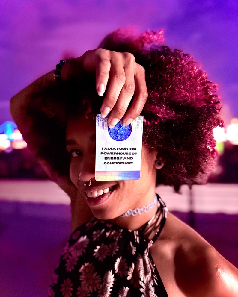 May include: A rectangular affirmation card featuring a blue disco ball graphic at the top and the text I AM A FUCKING POWERHOUSE OF ENERGY AND CONFIDENCE! printed in black, with a colorful grid pattern at the bottom edge against a white background.