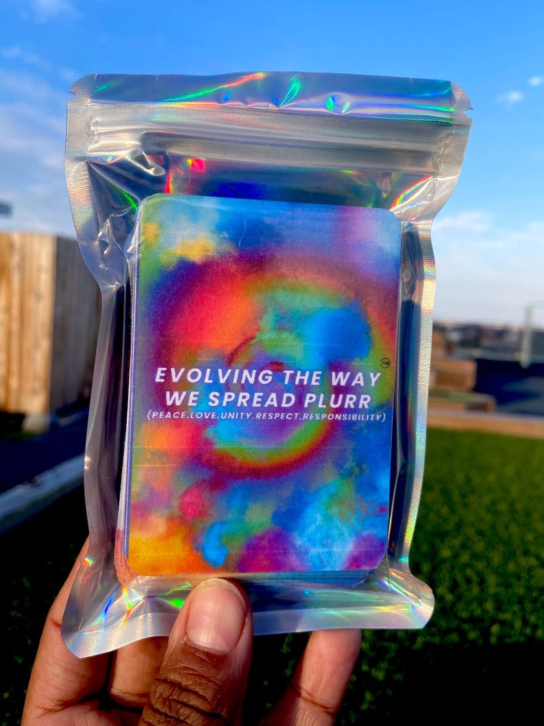 May include: A rectangular deck of cards with a vibrant tie-dye pattern in shades of blue, yellow, and red, enclosed in a holographic resealable plastic pouch. The text reads: EVOLVING THE WAY WE SPREAD PLURR (PEACE, LOVE, UNITY, RESPECT, RESPONSIBILITY).
