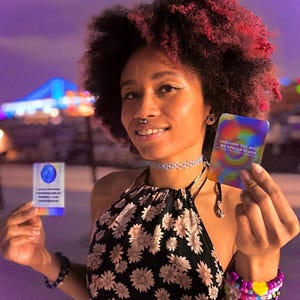 May include: Two rectangular cards with holographic finishes. The left card features a blue circular graphic and text. The right card displays a colorful swirl pattern with the text "EVOLVING THE WAY WE SPREAD PLUR" printed in white.