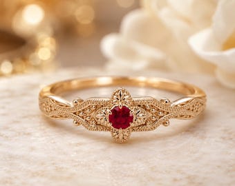 May include: A gold ring featuring a central round-cut red ruby gemstone. The band displays intricate metalwork with a textured, filigree-inspired pattern surrounding the stone, creating a detailed and ornate appearance on the metal surface.