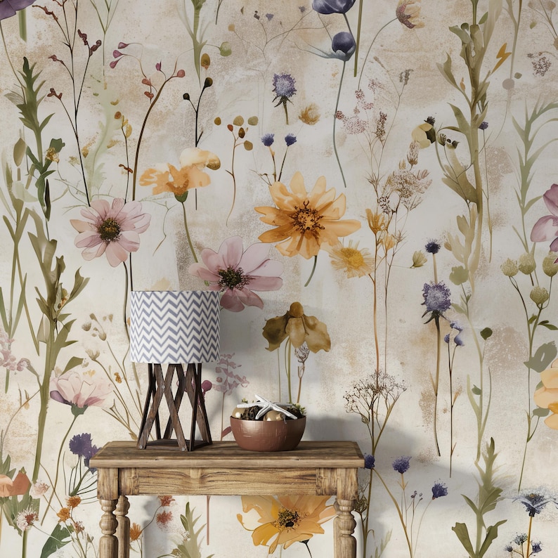 Puede incluir: Una mesa de madera con una l&aacute;mpara peque&ntilde;a y un cuenco con objetos decorativos se encuentra frente a un papel pintado floral. La l&aacute;mpara tiene una pantalla con un patr&oacute;n de chevron gris y blanco. El papel pintado presenta flores de acuarela en tonos amarillos, rosas y morados.
