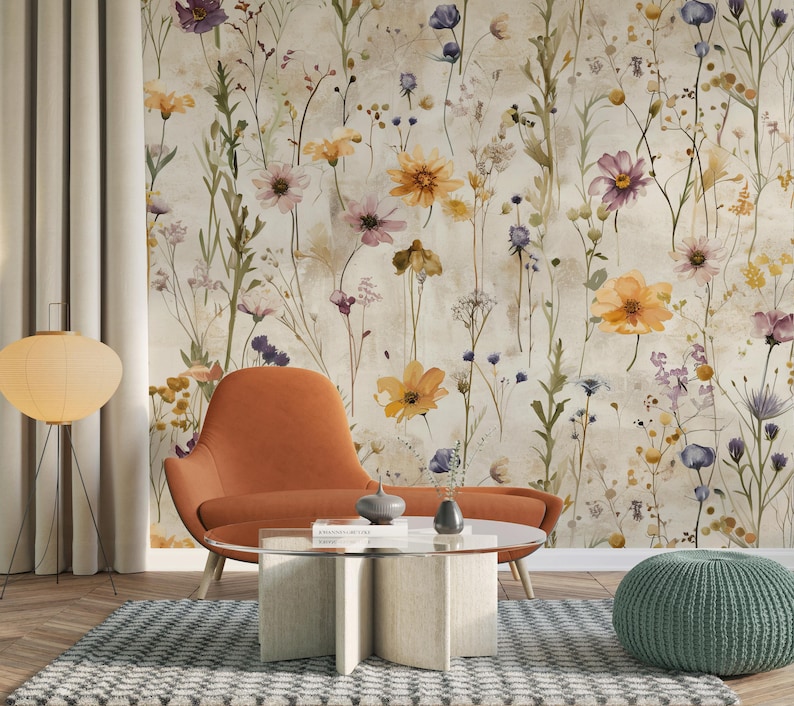 Puede incluir: Un sill&oacute;n naranja y una mesa de centro con tapa de cristal y base beige est&aacute;n frente a un papel pintado floral. Un puf verde y una l&aacute;mpara de pie con pantalla redonda de papel tambi&eacute;n est&aacute;n en la habitaci&oacute;n. El papel pintado presenta flores coloridas.