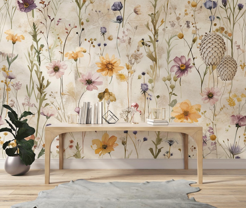 Puede incluir: Una mesa de madera clara frente a un papel pintado floral con flores de acuarela en tonos amarillos, morados y rosas. Una planta en maceta y libros est&aacute;n sobre la mesa. Una alfombra gris est&aacute; en el suelo.