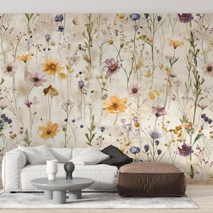 Puede incluir: Papel pintado floral con un dise&ntilde;o de acuarela de flores silvestres en tonos amarillos, morados y rosas. Las flores se colocan sobre un fondo neutro, creando una est&eacute;tica suave. La imagen tambi&eacute;n muestra un sof&aacute; blanco, una mesa de centro y un puf marr&oacute;n.