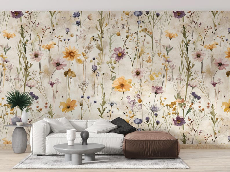 Puede incluir: Papel pintado floral con un dise&ntilde;o de acuarela de flores silvestres en tonos amarillos, morados y rosas. Las flores se colocan sobre un fondo neutro, creando una est&eacute;tica suave. La imagen tambi&eacute;n muestra un sof&aacute; blanco, una mesa de centro y un puf marr&oacute;n.