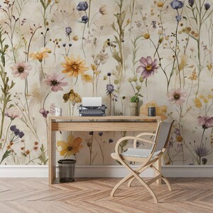 Puede incluir: Un escritorio de madera clara con una m&aacute;quina de escribir antigua, una peque&ntilde;a planta en maceta y una vela decorativa se encuentra frente a un papel pintado floral. Una silla de madera con asiento gris est&aacute; colocada frente al escritorio. Una papelera peque&ntilde;a est&aacute; en el suelo.