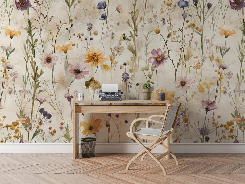 Puede incluir: Un escritorio de madera clara con una m&aacute;quina de escribir antigua, una peque&ntilde;a planta en maceta y una vela decorativa se encuentra frente a un papel pintado floral. Una silla de madera con asiento gris est&aacute; colocada frente al escritorio. Una papelera peque&ntilde;a est&aacute; en el suelo.