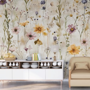 Puede incluir: Un papel pintado floral con flores de acuarela en tonos amarillos, morados y rosas. Las flores se colocan sobre un fondo neutro. Un mueble blanco con vajilla y un sill&oacute;n beige est&aacute;n frente al papel pintado.