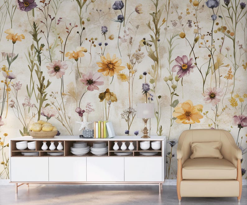 Puede incluir: Un papel pintado floral con flores de acuarela en tonos amarillos, morados y rosas. Las flores se colocan sobre un fondo neutro. Un mueble blanco con vajilla y un sill&oacute;n beige est&aacute;n frente al papel pintado.