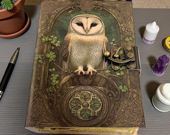May include: A detailed journal with a barn owl illustration on the cover. The cover features a brass clasp and intricate Celtic knotwork design. The owl is perched on a branch with green shamrocks. The journal is brown and green.